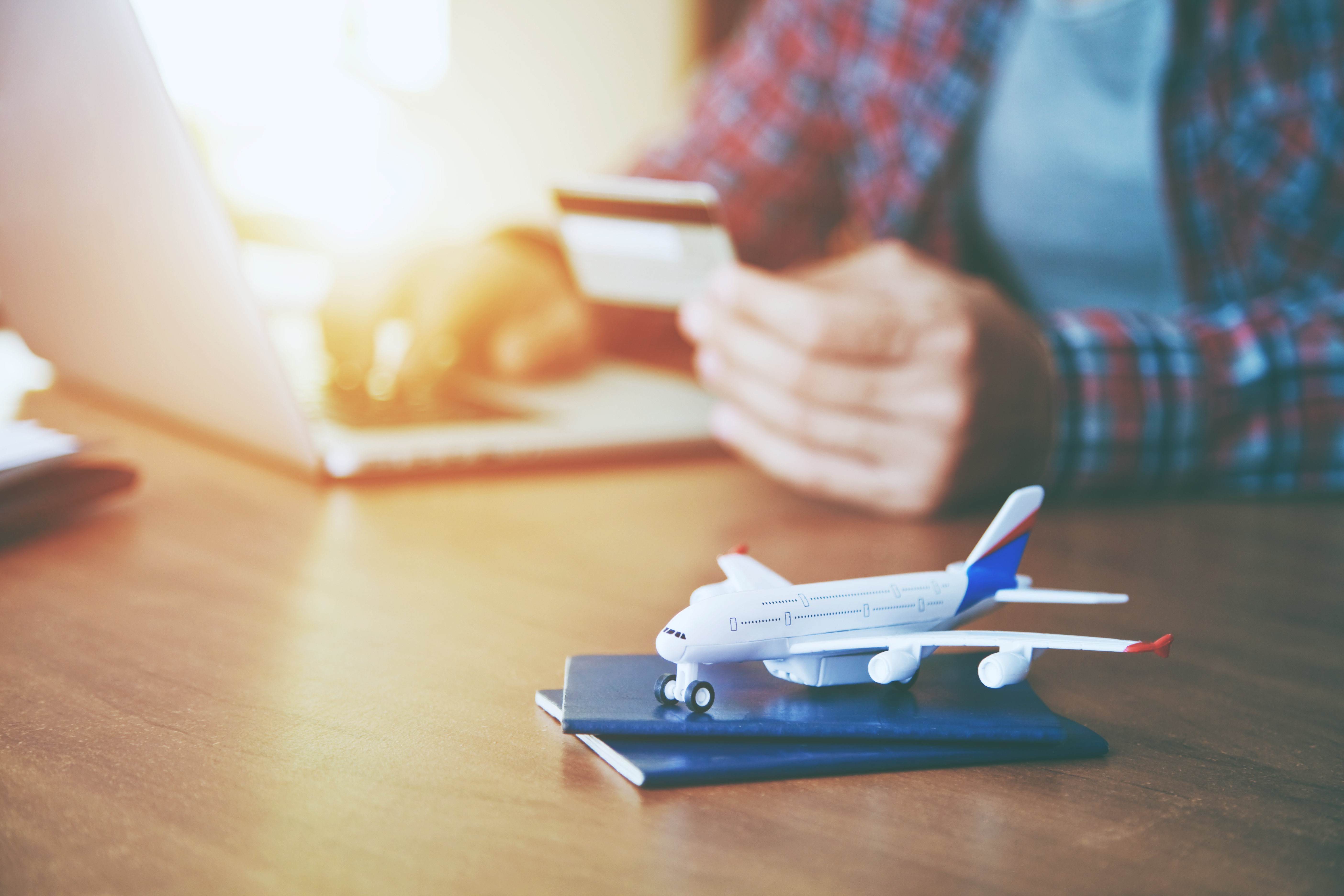 A man books a trip on a computer with his credit card. A toy airplane sits on a passport in the foreground