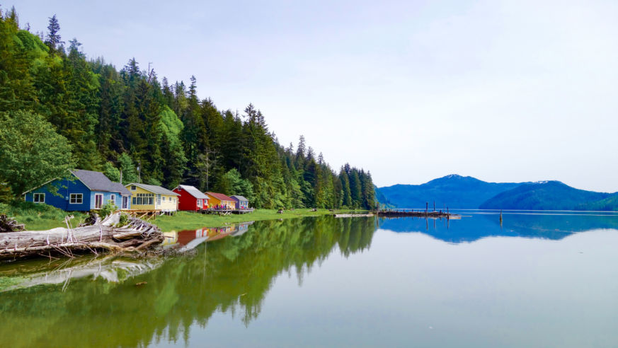 A lake with mountains in the horizon and colorful cottages on the left bank