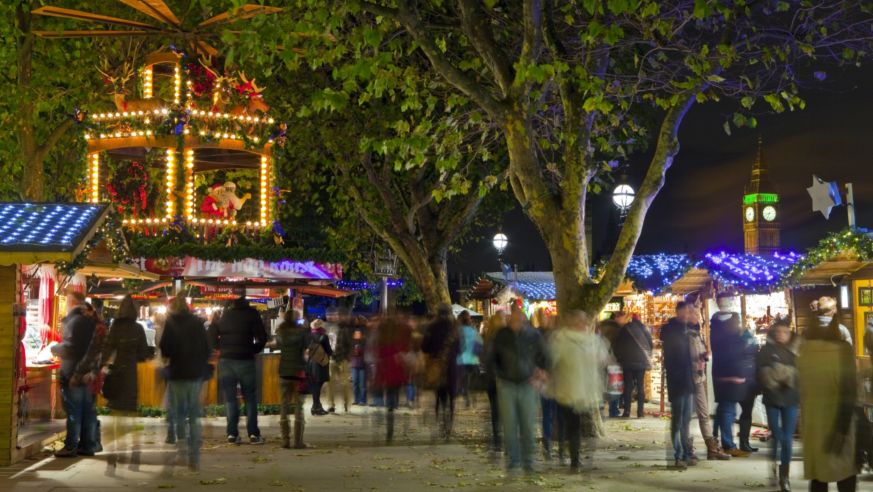 Pedestrians mill about a beautiful Christmas Market on the South Bank in London, with the Elizabeth Tower visible in the background.