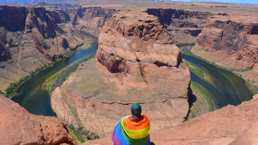 Mikah Meyer wearing a rainbow pride flag as he looks out over Horseshoe Bend