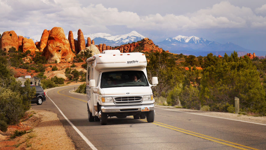 An RV drives past red rocks in Arches National Park, Utah.