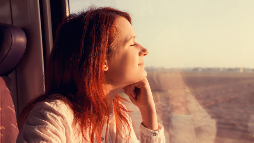 A young woman looks relaxed and satisfied as she looks out a train window while traveling