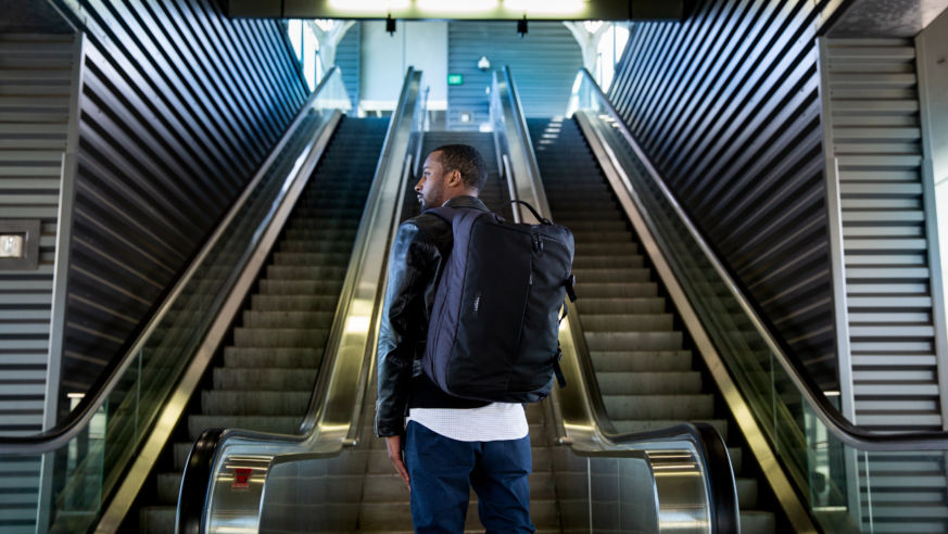 man with backpack at bottom of escalator