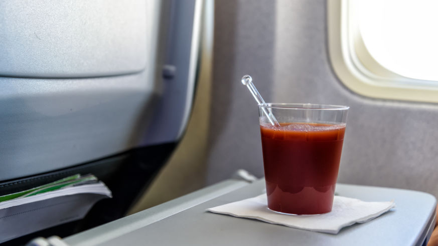 A view of a glass of tomato juice on an airplane tray.