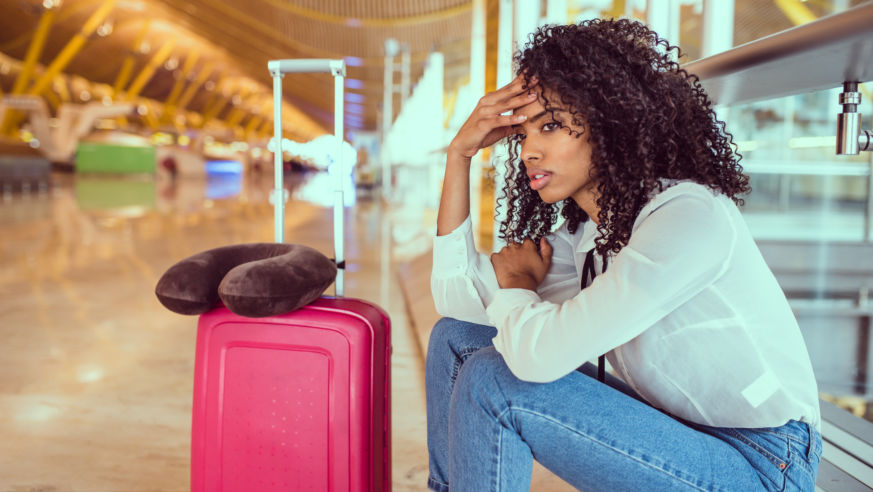 View of a woman sitting at an airport baggage carousel looking frustrated.