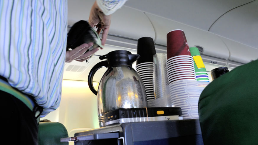 A view of a flight attending pouring coffee from a cart.