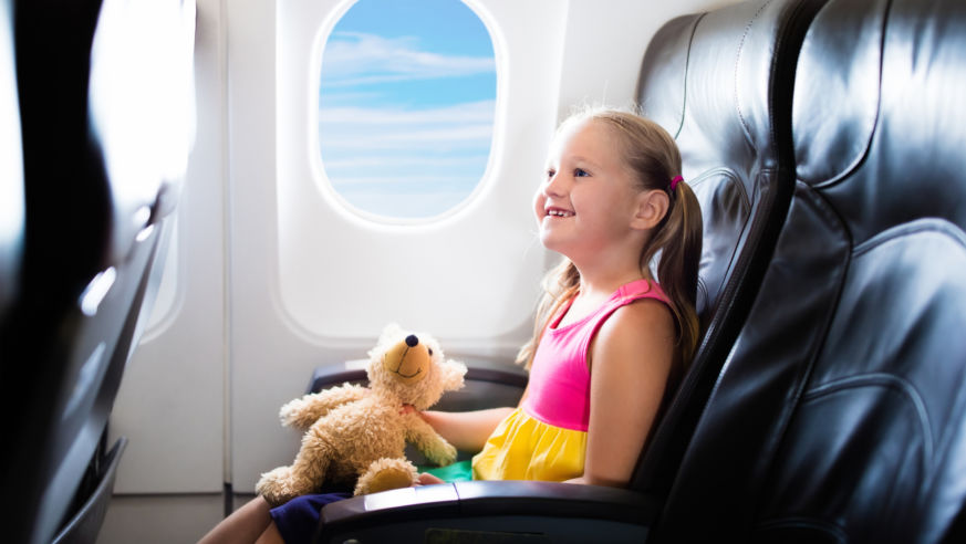 Little girl holding a teddy bear in an airplane window seat