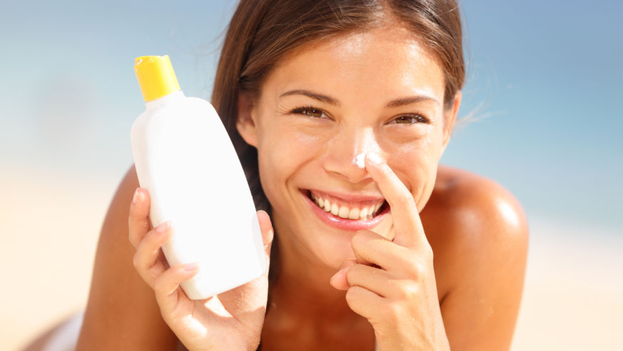 A smiling woman applying sunscreen