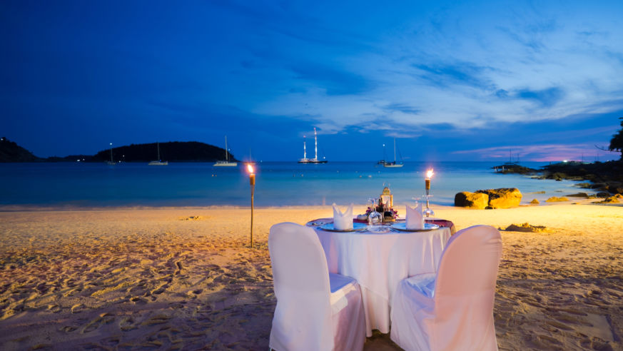 A romantic table with candles on a beach.