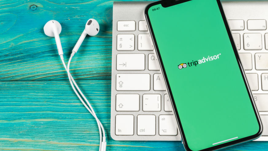An overhead view of an iPhone with the TripAdvisor app and a laptop