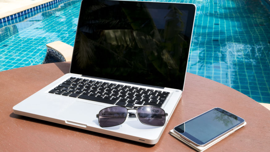 A view of a swimming pool with a laptop, smartphone, and sunglasses in the foreground.