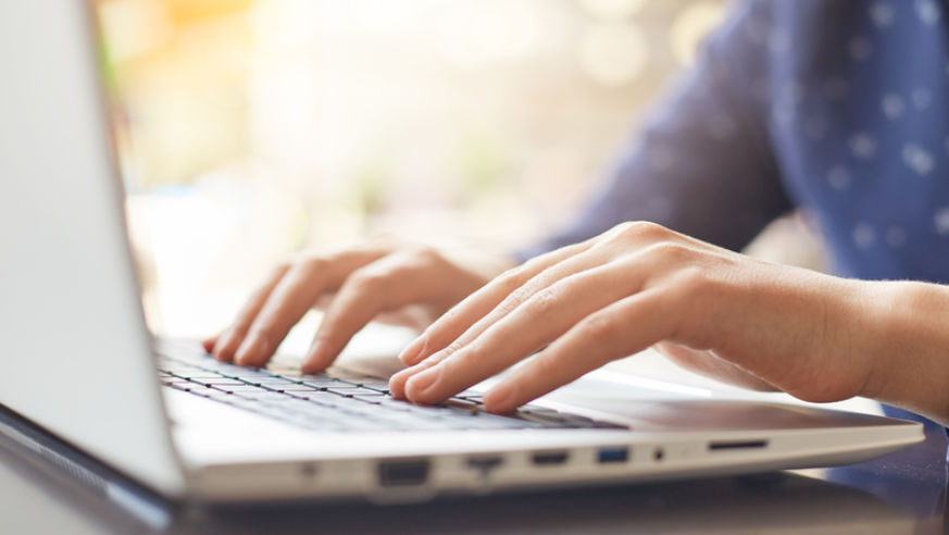 View of a laptop on. wooden desk and a woman's hands typing.