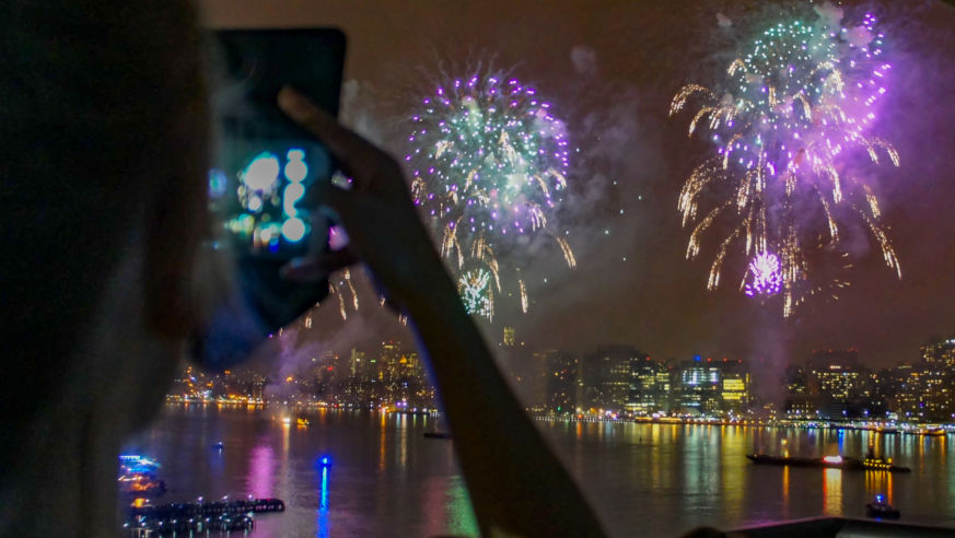 A view of New York City's 4th of July fireworks with a cellphone photographer in the foreground.
