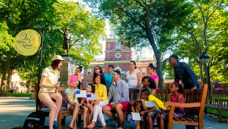 Professional storyteller entertains families on a bench in Philaderlphia