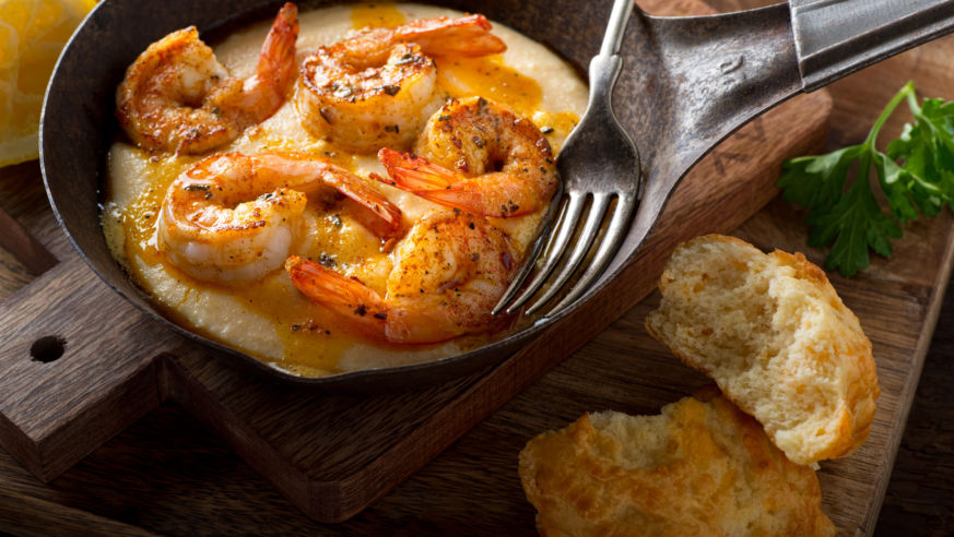 An overhead view of a plate of shrimp and grits with a cheddar biscuit on the side.