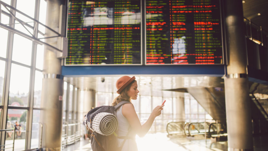 A solo traveler looks at her smartphone at the airport.