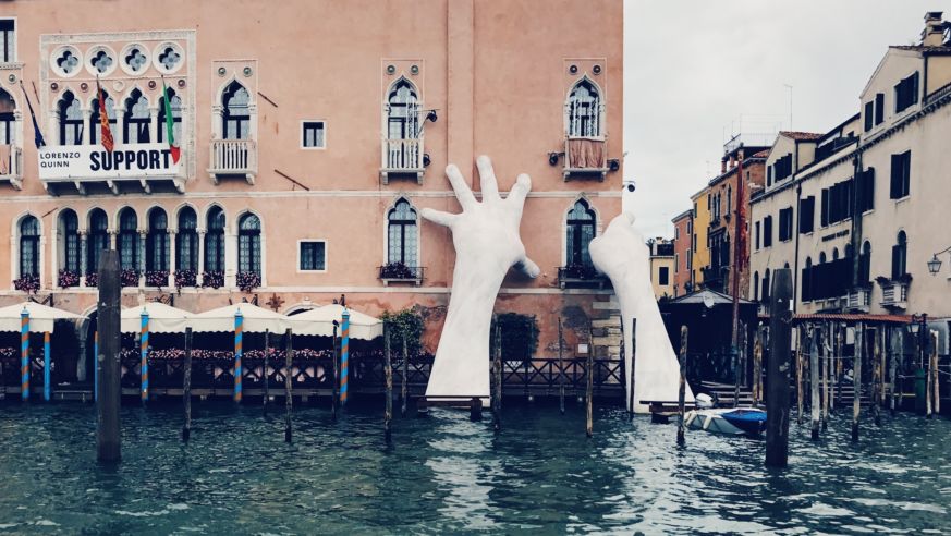 Giant sculpture hands rise from a Venice Canal.