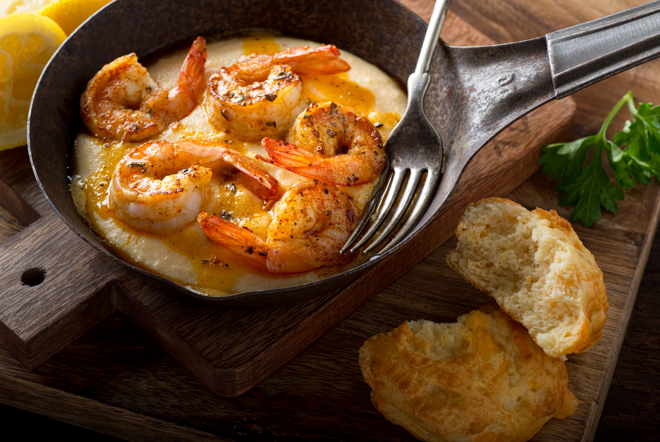An overhead view of a plate of shrimp and grits with a cheddar biscuit on the side.