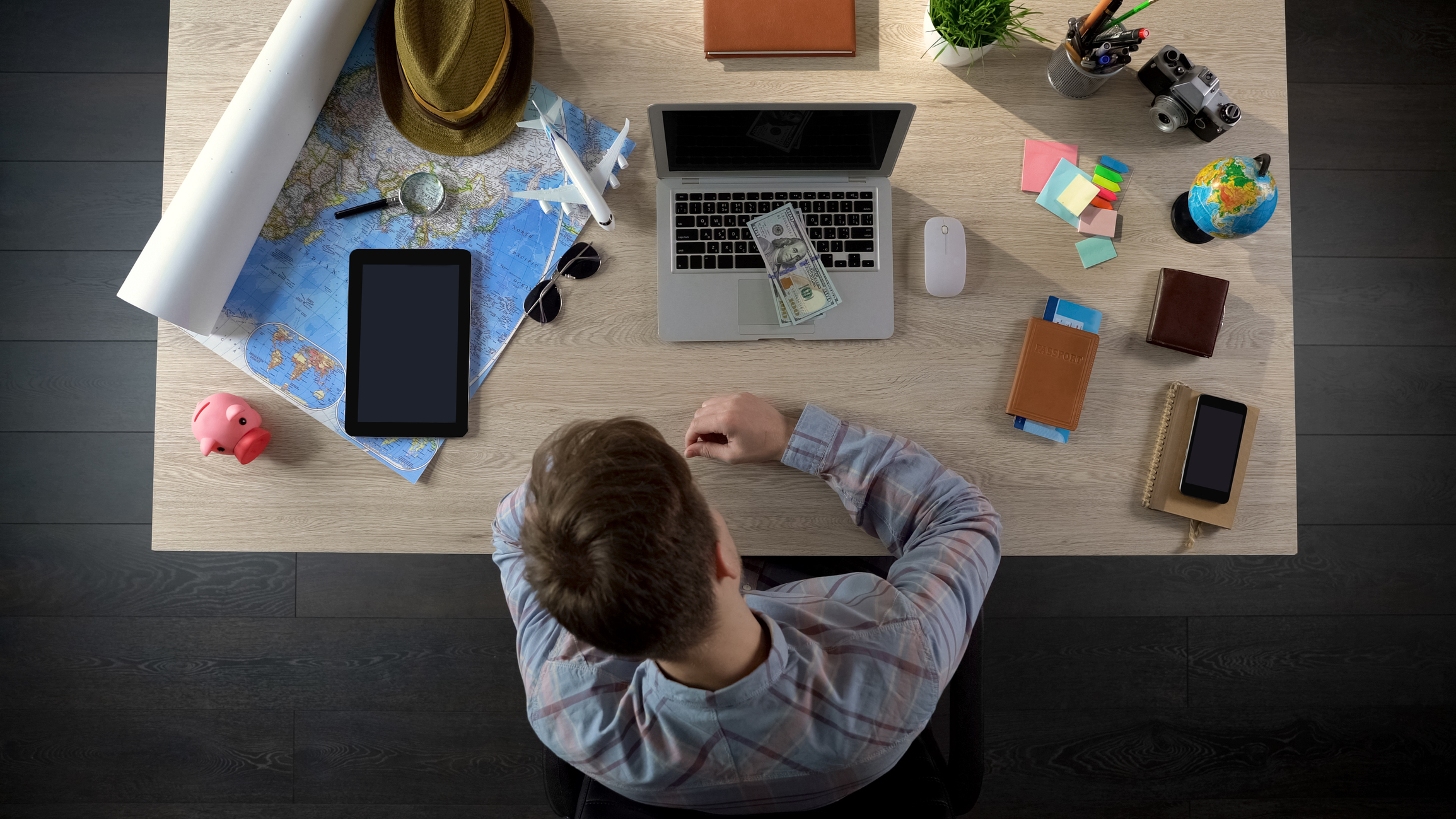 Man at desk with laptop, money, and other tools for trip planning.